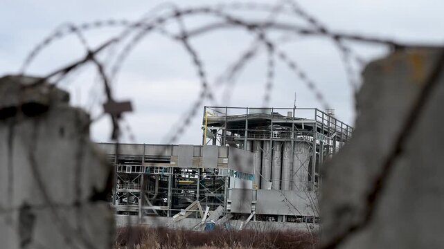 A destroyed factory on the outskirts of Kramatorsk is seen through a broken fence and tangled barbed wire. A stark view of the industrial damage caused by the war in Ukraine.
