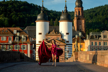 schöne Frau in rotem Kleid, tanzt in Heidelberg in der Morgensonne, über die alte Brücke.
