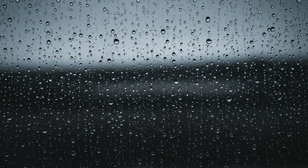 Raindrops cover a window blurring a grayscale landscape behind