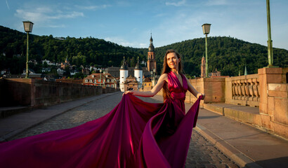 schöne Frau in rotem Kleid, tanzt in Heidelberg in der Morgensonne, über die alte Brücke.