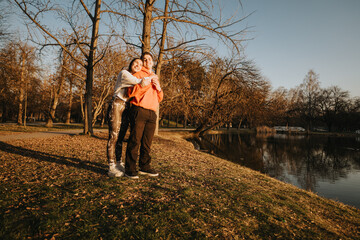 Fototapeta premium A couple enjoying a cozy moment together under golden sunlight by a serene park lake, surrounded by trees capturing the essence of autumn.