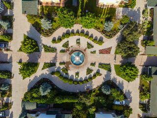 A top-down aerial view of a resort's decorative garden with a central fountain, hedges, flowers, and walkways