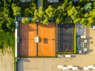 A top-down aerial view of a resort's tennis and basketball courts next to a sandy beach area