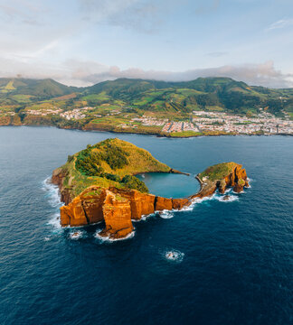 Aerial view of the islet's volcanic crater embracing a serene lagoon, framed by rugged cliffs and the distant town, Ilh&Atilde;&copy;u de Vila Franca do Campo, A&Atilde;&sect;ores, Portugal.