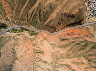 A top-down aerial view of a road winding through a dry, rugged, and heavily eroded landscape near a small village