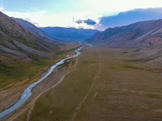 A wide aerial shot of a river winding through a large mountain valley at dusk, with soft light and a vast, open landscape