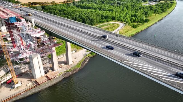 Aerial shooting of bridge construction along existing A7 motorway bridge crossing Kiel Canal near Rendsburg with ongoing engineering work with scaffolding, cranes, pillars next to highway with traffic