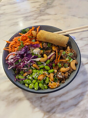Fresh and colorful Buddha bowl on a white marble tabletop, featuring edamame beans, shredded...