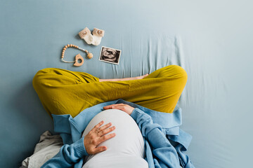 Pregnant woman touching her belly and looking at ultrasound image at home.