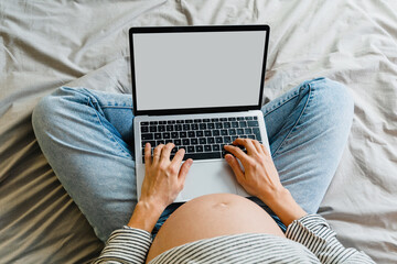 Pregnant woman using laptop at home. Pregnant belly of expectant mother with computer.