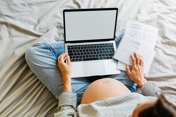 Naklejka premium Pregnant woman using laptop at home. Pregnant belly of expectant mother with computer.