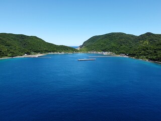 Obraz premium Crystal clear waters and rocky beach at Ikezuka, Naru Island, Goto Islands, Nagasaki, Japan – stunning summer coastline with lush green hills and transparent turquoise sea.