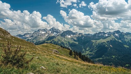Obraz premium Spectacular mountainous panorama adorned with fluffy clouds and rich green grasslands, highlighted by majestic snowy peaks afar.