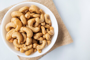 Top view piles of roasted tasty cashews in a white bowl on natural background