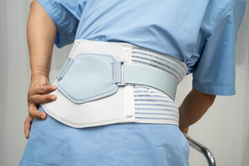 Asian senior pain back wearing elastic support belt with walker.