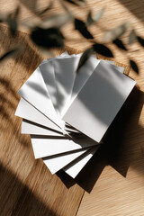 Stack of vertical white cards on wooden surface with bright sunlight and plant shadows. Natural minimal branding scene. Copy space included.
