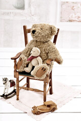 Vintage style photo of old teddy bear sitting on the chair in the room