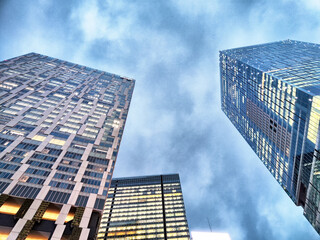 View of modern skyscrapers reaching towards a cloudy sky in an urban setting at dusk