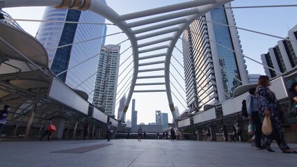 Time-lapse potential scene featuring pedestrians briskly crossing a footbridge with futuristic design elements amidst towering skyscrapers in Bangkok vibrant urban setting