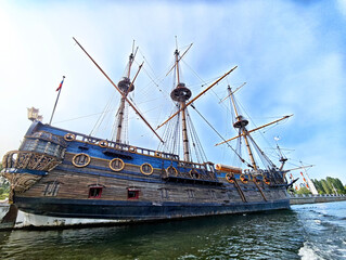 Historic wooden ship docked in calm waters on a bright sunny day with clear skies