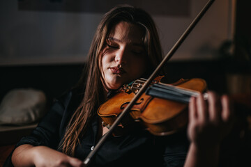 A young woman, deeply focused, plays the violin with concentration and dedication in a dimly lit...