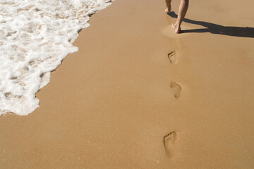 Barefoot footprints on sandy beach with ocean waves