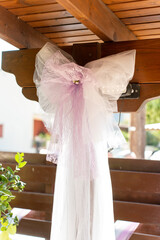 Decorative bow made of tulle adorns rustic wooden shelter at outdoor celebration venue during...
