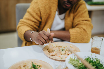 A cropped view of an individual in a yellow sweater, using a fork to eat food served on a plate amidst a casual dining setting.
