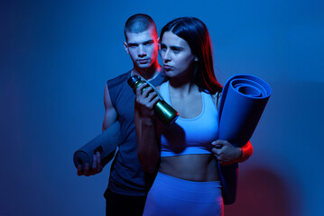 Couple preparing for a workout session in a studio with colorful lighting and fitness equipment in...