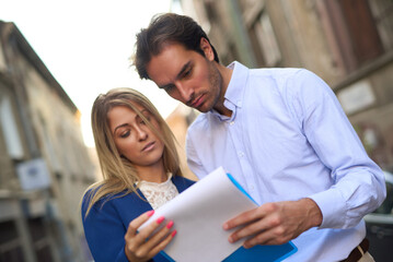 Couple reviews documents together on a charming street in an Italian town during late afternoon...
