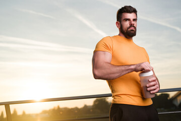 Muscular man preparing protein shake outdoors during sunset in urban setting