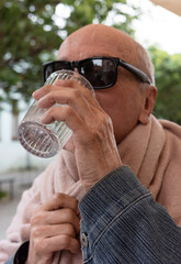 Older man taking a refreshing drink of water on a sunny day in nature.