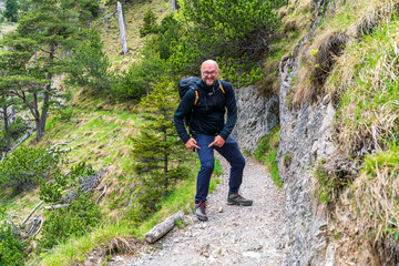 Happy Man with glasses and a black jacket and backpack along to the Bavarian hiking paths