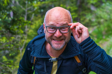 Happy Man with glasses and a black jacket and backpack along to the Bavarian hiking paths