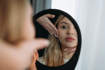 young woman looking in a mirror after facian rejuvenation procedure at aesthetic clinic
