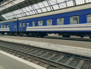 A blue passenger car standing on the platform, ready for departure. In the foreground, a railway track is visible, emphasizing the atmosphere of travel and anticipation.