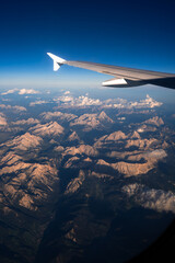Obraz premium Airplane wing view over mountain range with blue sky and clouds, aerial travel landscape from plane window.