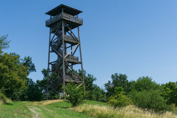 Tall wooden observation tower on a grassy hill under a clear blue sky, concept of hiking, lookout...