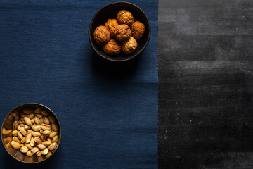 Black bowl with walnuts and blue table cloth on black chalkboard background. Flat lay. Top view.