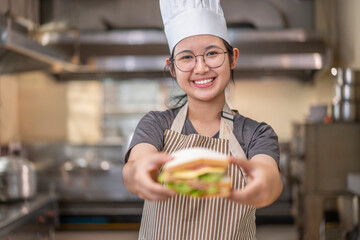 Smiling Asian Female Chef Holding Sandwich in Kitchen