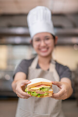 Smiling Asian Female Chef Holding Sandwich in Kitchen