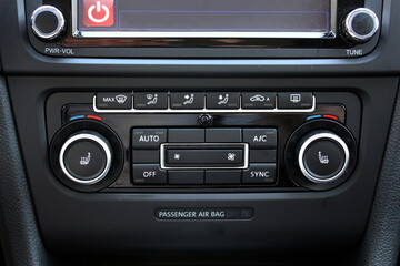 Close-up of a car climate control panel featuring dual temperature dials, buttons for air...