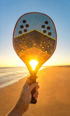 Peaceful sunset sky reflecting on the ocean with beach tennis racket and ball in the foreground. Represents outdoor activity and tropical seaside mood.