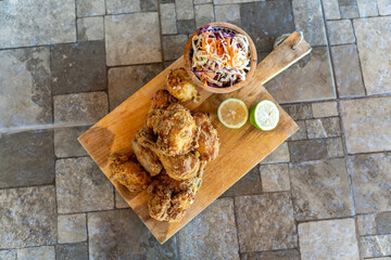 Fried chicken served with coleslaw and lime on a rustic wooden board