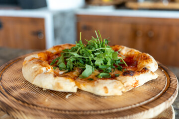 Delicious homemade pizza topped with fresh greens placed on a wooden serving board in a cozy...
