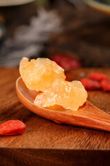 Handmade large grain yellow icing sugar resting on a wooden spoon amidst scattered goji berries on...