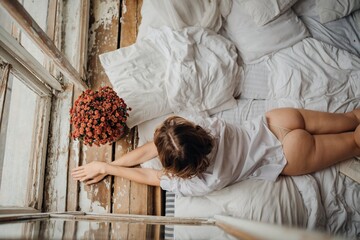 sexy woman in white shirt in bed by the window with a bouquet. naked buttocks