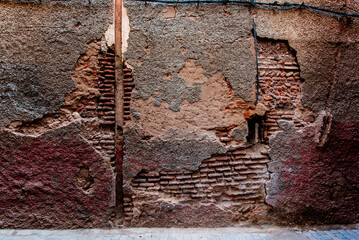Weathered wall in Marrakech, Morocco, showing cracked plaster and exposed bricks. A gritty texture...