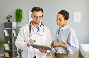 Portrait of a young african american woman patient in medical office listening to male doctor...