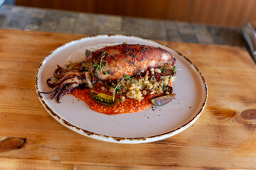 Grilled squid served on a rustic plate with vegetables and sauce at a seaside restaurant in late afternoon